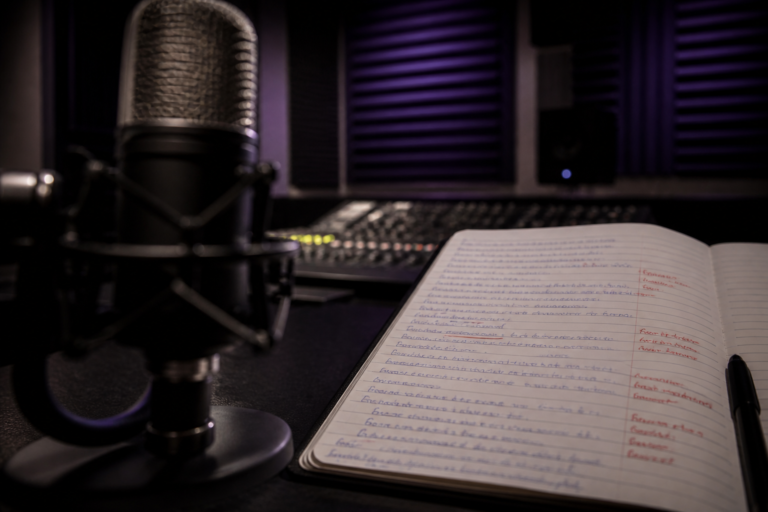 Microfone de estúdio ao lado de caderno de transcrição aberto com correções na margem